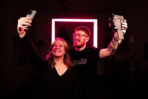 Joel och Mathilda står framför en lysande rosa led-fyrkant. mathilda tar en selfie med mobil och Joel tar en selfie med kamera